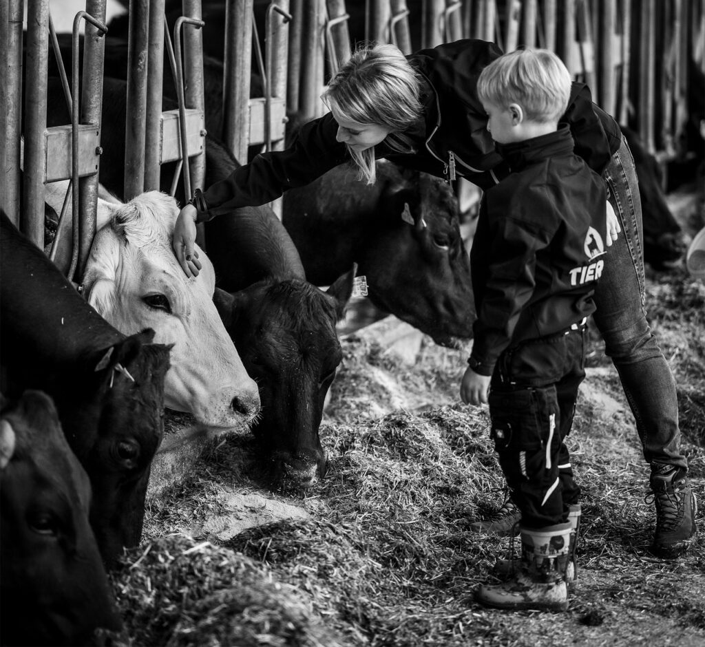 Bauer und Kinder streicheln Rinder im Stall in Tirol
